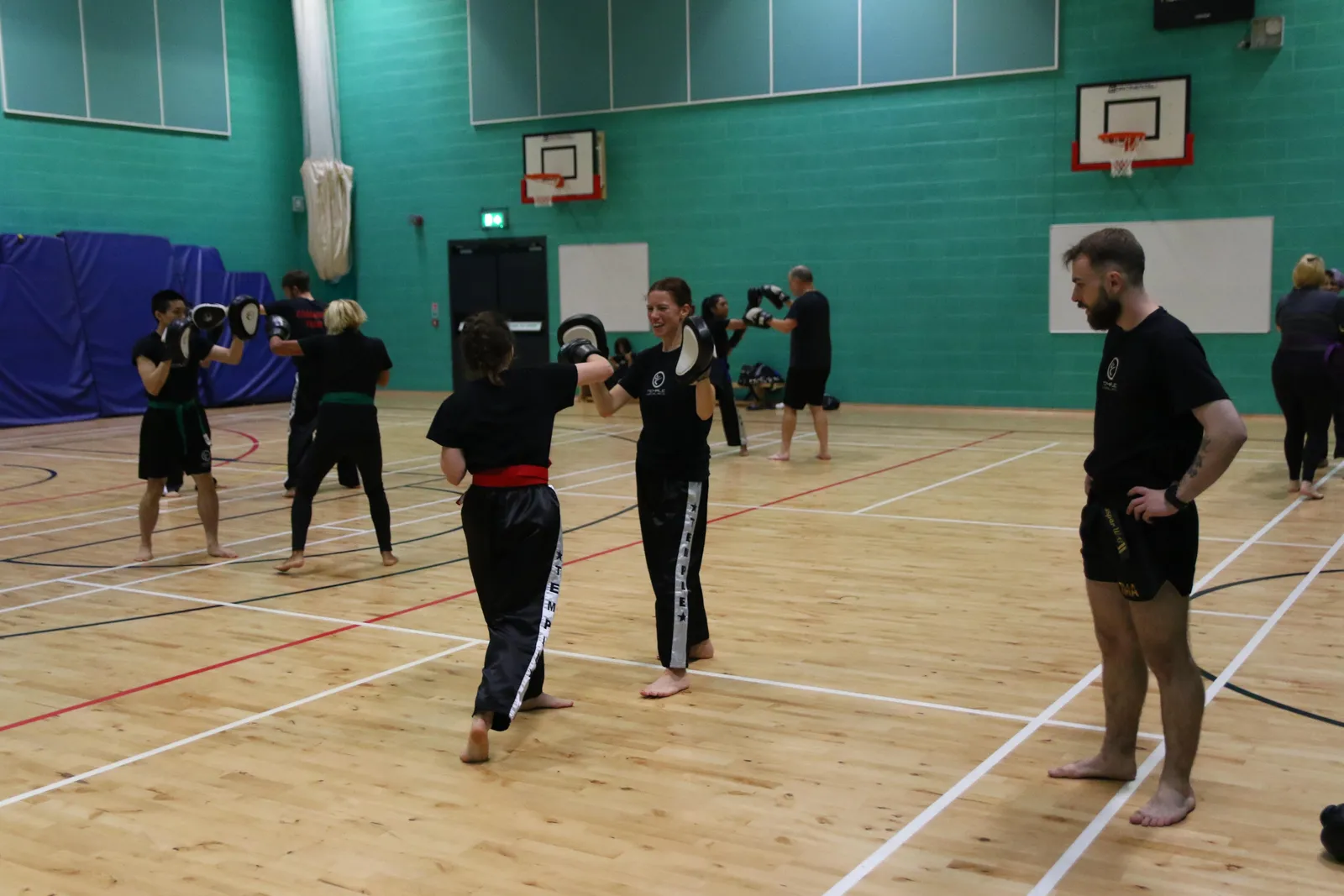Adults pairing up for pad work in a sports hall